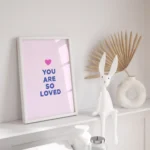 Framed pink print with 'You Are So Loved' message with rabbit figurine on shelf
